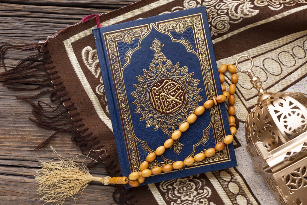 Al-Qur’an berwarna biru dengan hiasan keemasan diletakkan di atas sajadah cokelat, dihiasi tasbih kayu dan lentera islami di sampingnya.