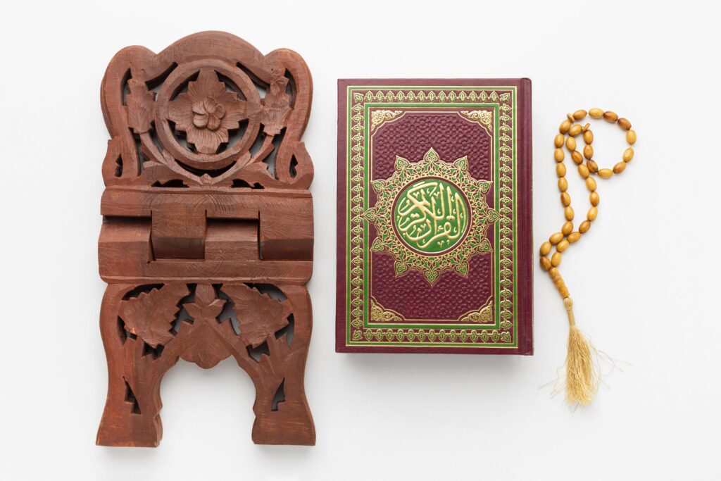 Al-Qur’an dengan sampul merah, rehal kayu, dan tasbih di atas latar putih sebagai simbol literasi Qur’ani.